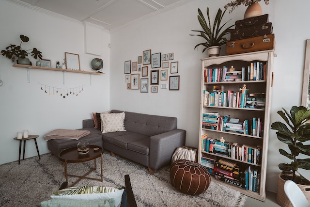 a sofa in a corner next to a bookshelf surrounded by frames